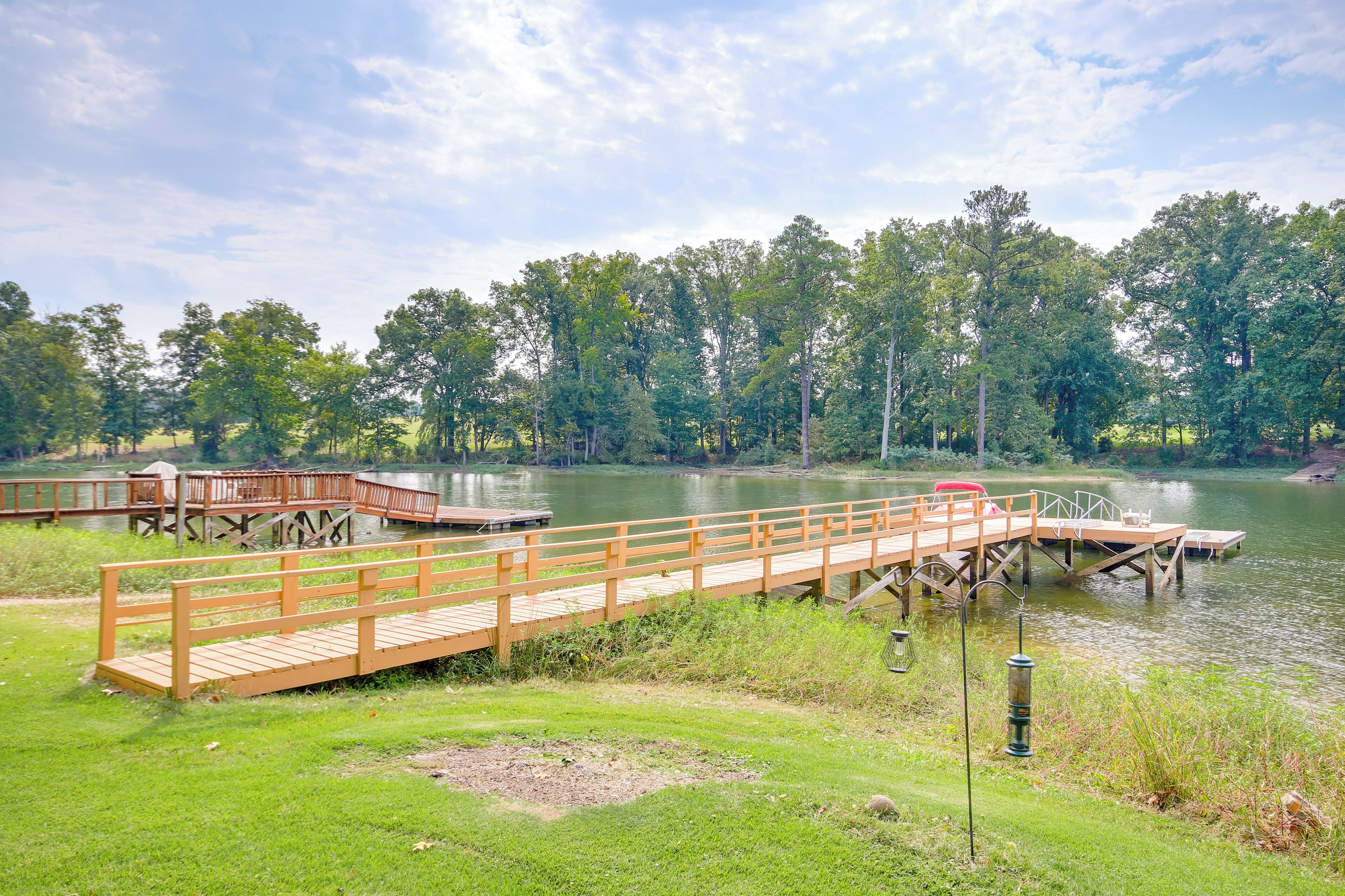 A wooden bridge over a calm lake, surrounded by lush greenery and trees.