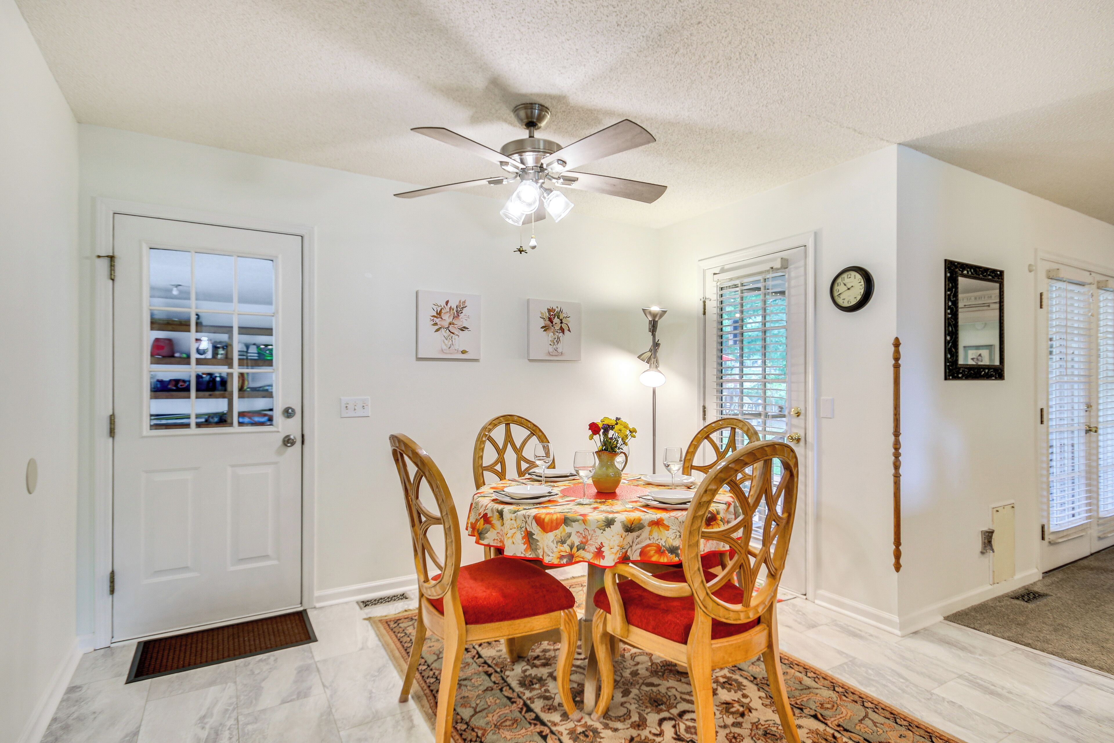 A dining area with a ceiling fan, a table with chairs, a vase with flowers, and a clock on the wall.