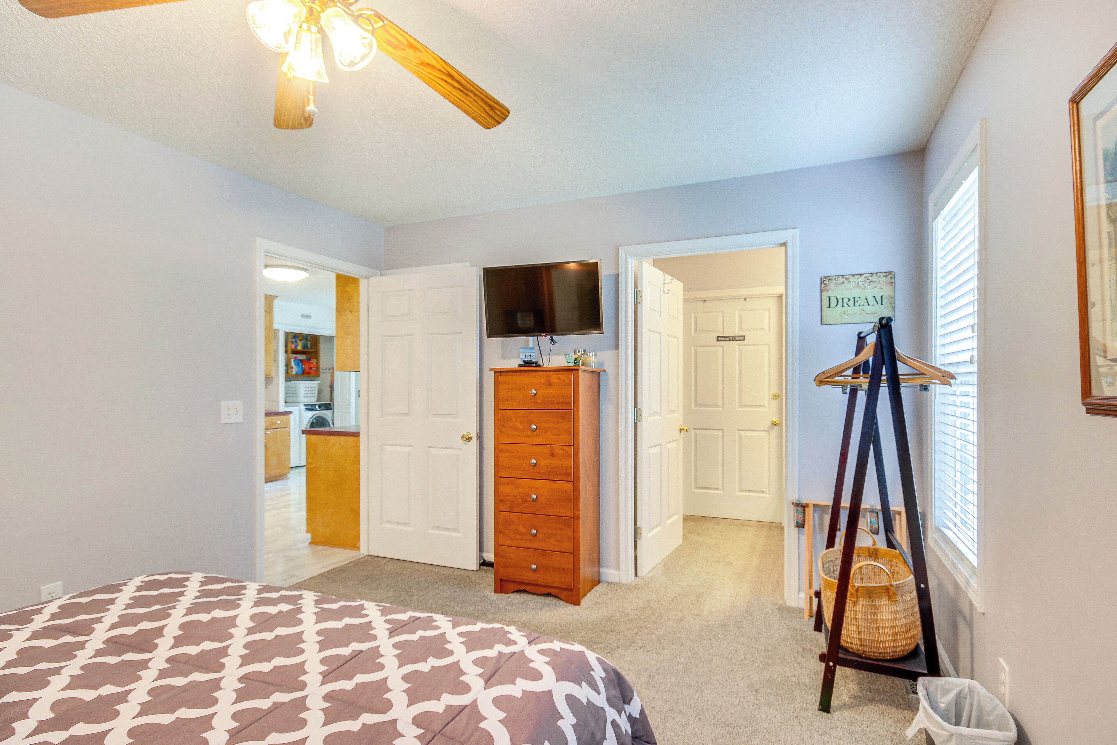 A bedroom with a bed, dresser, TV, and a wall-mounted shelf.