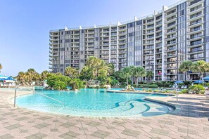 A large swimming pool surrounded by a landscaped area with palm trees and a multi-story hotel building in the background. - Nautical Edgewater Resort Condo - Walk to Beaches! (Panama City Beach)