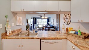 A kitchen with white cabinets, a granite countertop, and a dishwasher. There is a dining area visible through the kitchen.