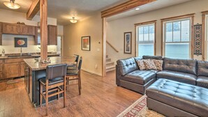 A spacious living area with a large leather sectional sofa, a wooden dining table with chairs, and a kitchen with wooden cabinets. - Updated Townhome w/ Hot Tub - Walk to Downtown! (Red Lodge)