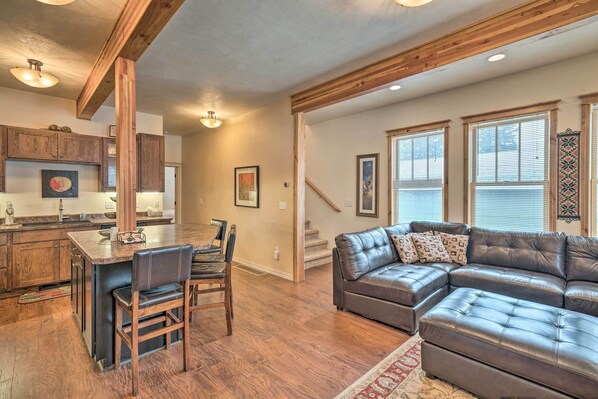 A spacious living area with a large leather sectional sofa, a wooden dining table with chairs, and a kitchen with wooden cabinets.