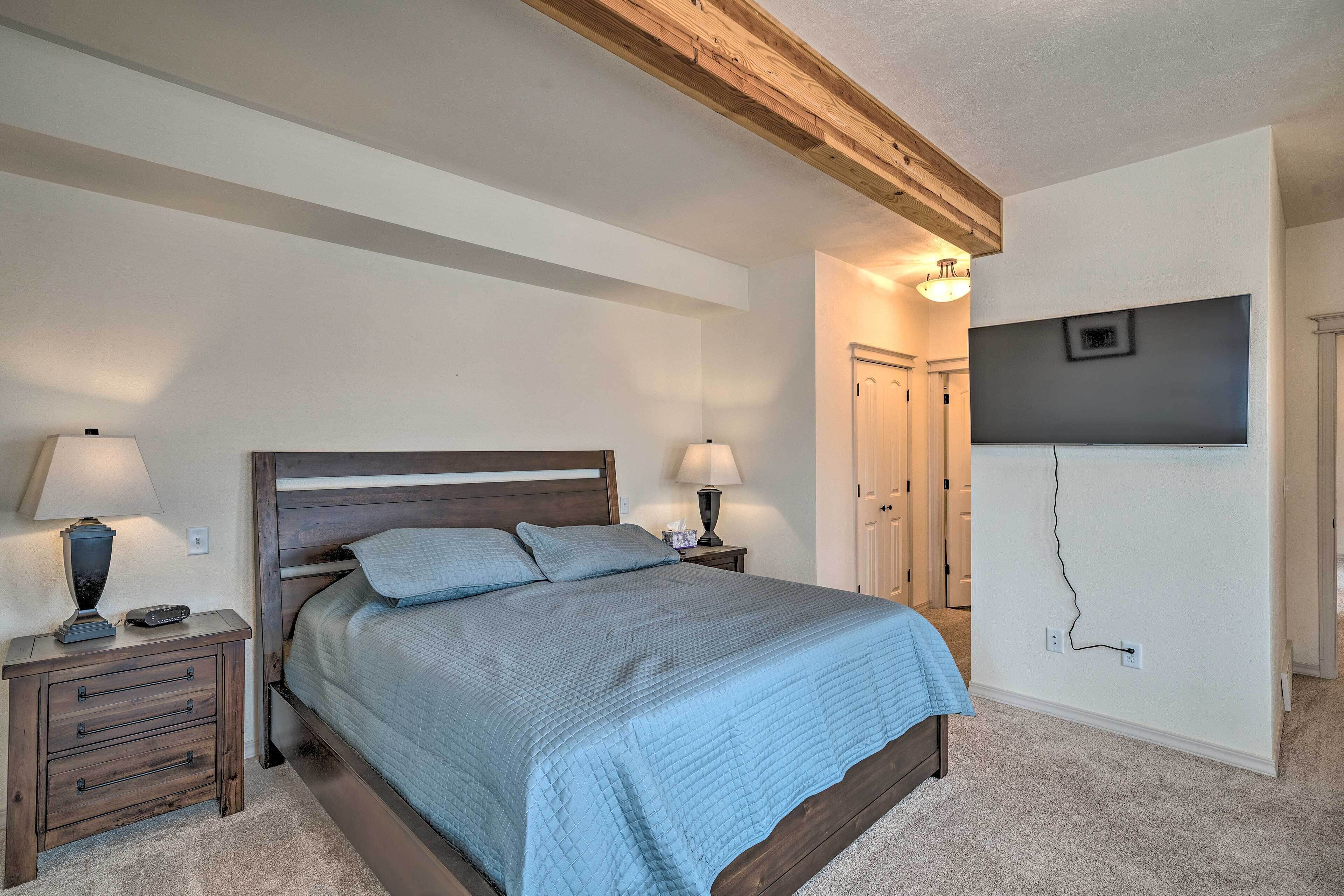 A bedroom with a bed, nightstands, a TV mounted on the wall, and a door in the background.