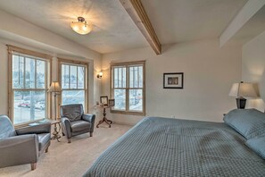 Een slaapkamer met een groot bed, twee fauteuils, een tafeltje en een raam met jaloezieën.