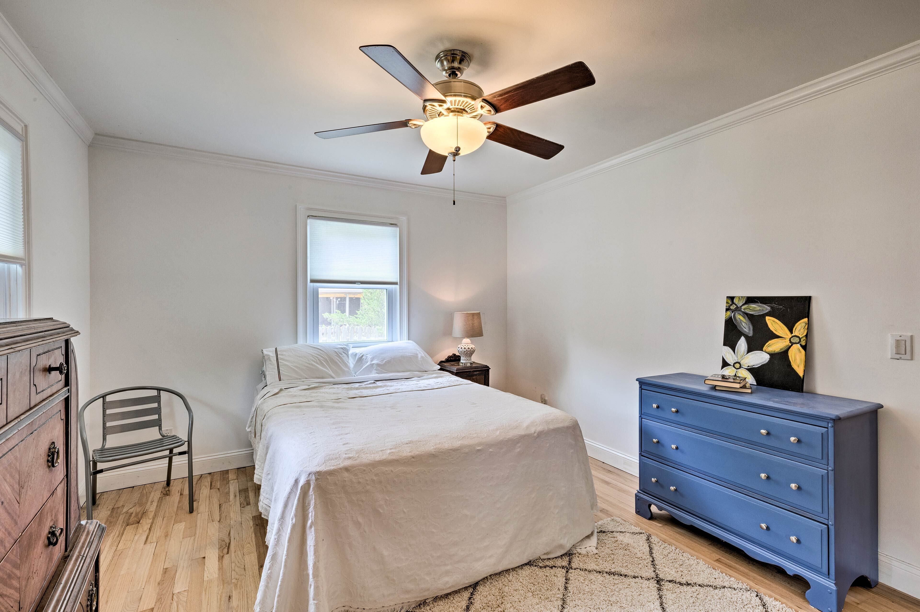 A bedroom with a bed, a dresser, a chair, a ceiling fan, and a window.