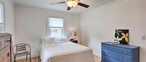 A bedroom with a bed, a dresser, a chair, a ceiling fan, and a window.
