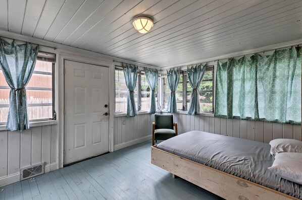 A bedroom with a wooden bed, a chair, and a window with curtains.