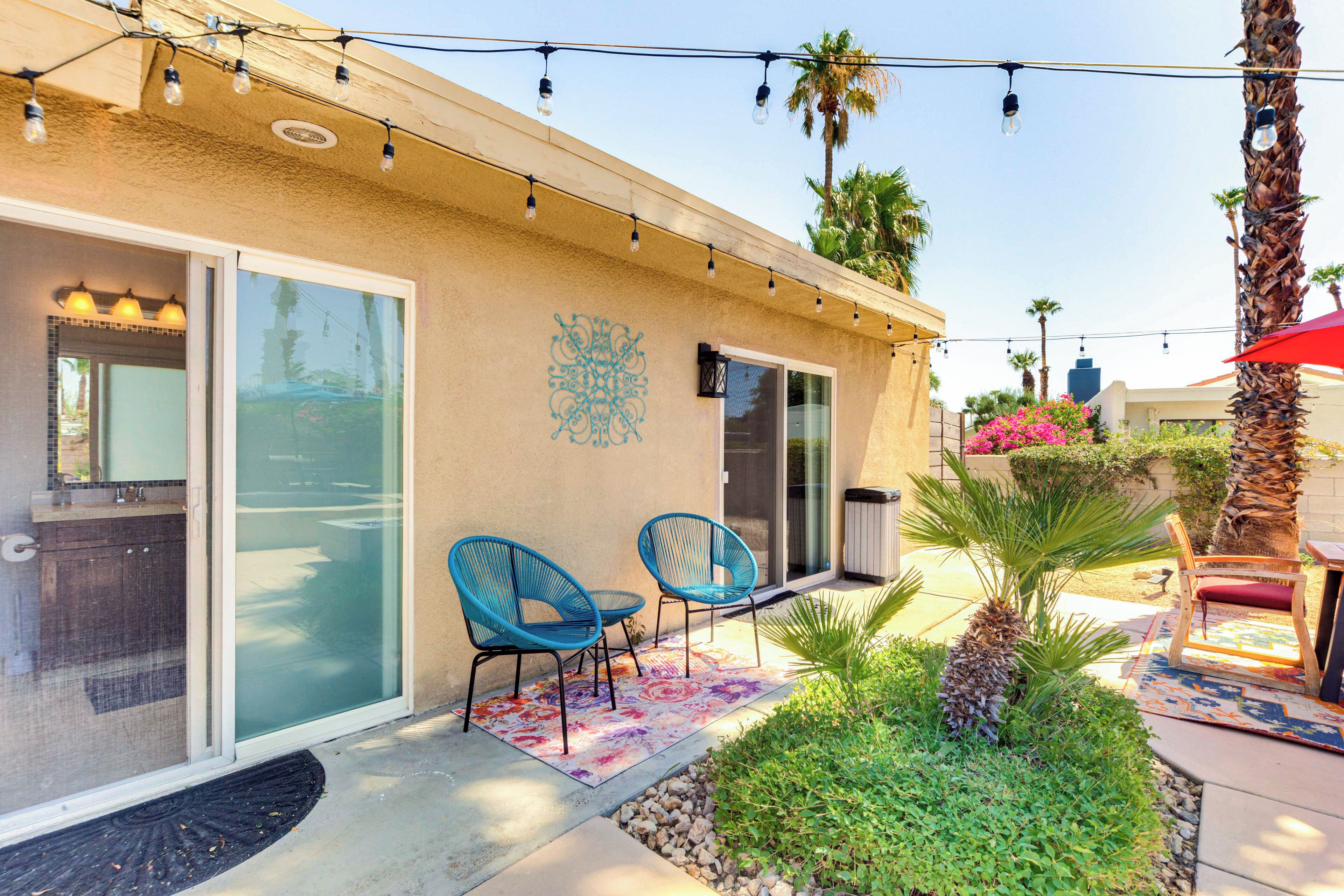 A patio area with two blue chairs, a palm tree, and a red umbrella.