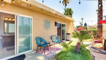 A patio area with two blue chairs, a palm tree, and a red umbrella.