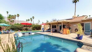 A swimming pool with lounge chairs and umbrellas, surrounded by palm trees and a building with a patio. - Private Pool & Putting Green: Palm Springs Home! (Palm Springs)
