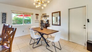 A dining area with a wooden table, white chairs, a chandelier, and a view of greenery outside. - Private Pool & Putting Green: Palm Springs Home! (Palm Springs)