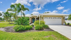 A residential house with a garage, a front yard with palm trees and shrubs, and a clear blue sky. - Pool, Lake & Sunset Views: Home in Sarasota (Sarasota)