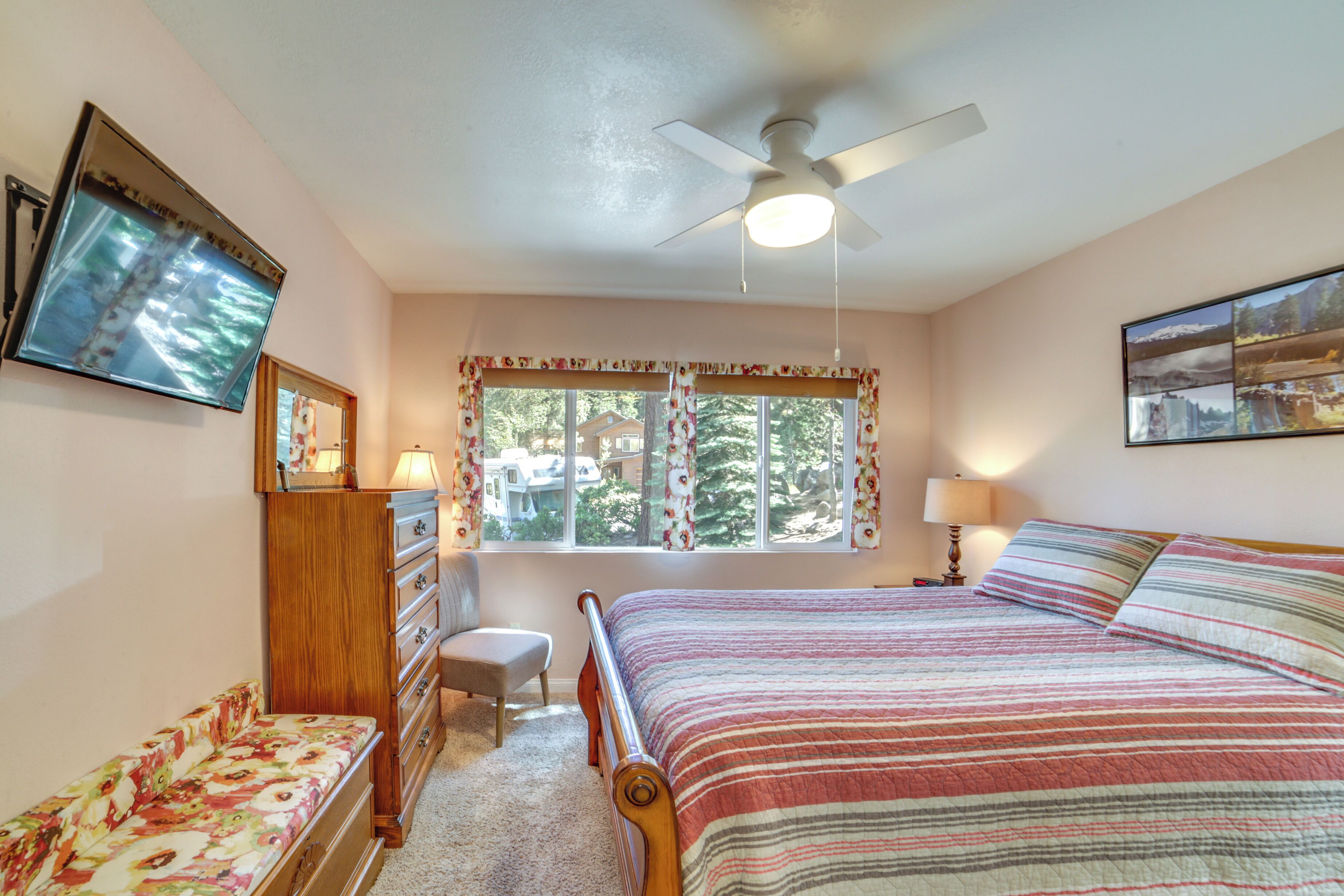 A bedroom with a bed, a desk, a chair, a window with curtains, and a ceiling fan.