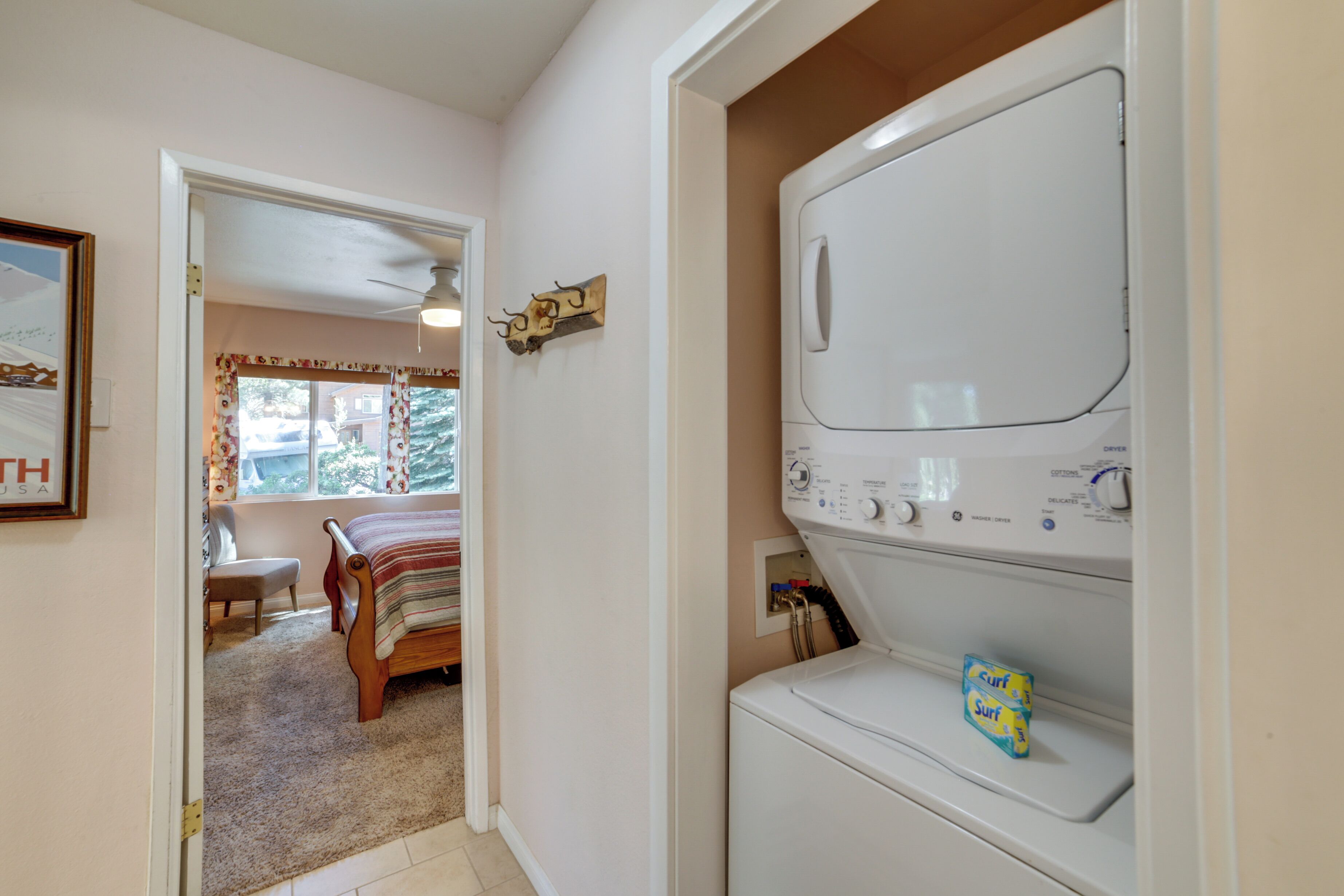 A laundry room with a front-loading washer and dryer, a bench, and a door leading to another room.