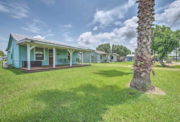 A row of light blue houses with a porch, a grassy lawn, and a palm tree.