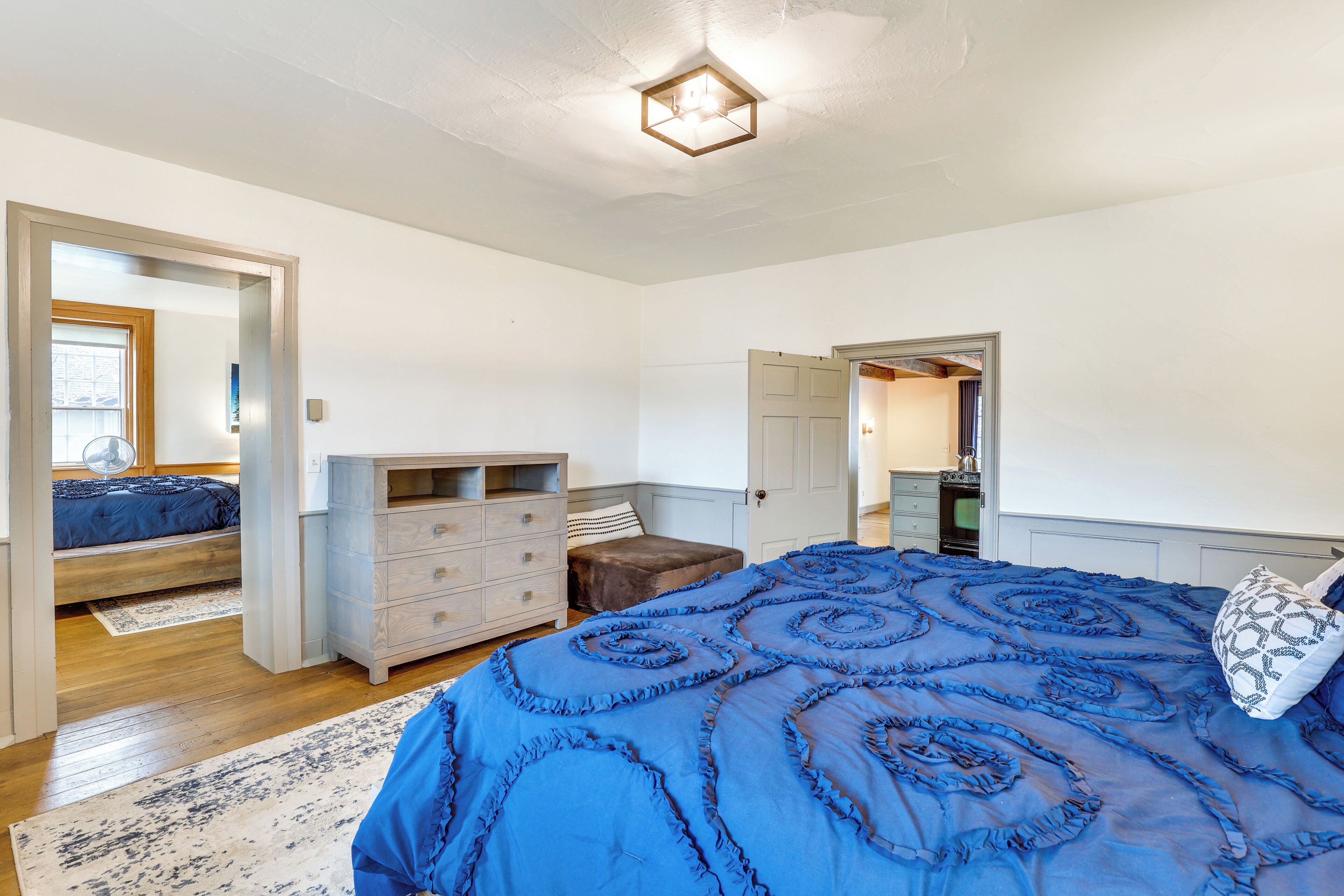 Un dormitorio con una cama grande, un aparador, una mesita de noche y una puerta que da a otra habitación.