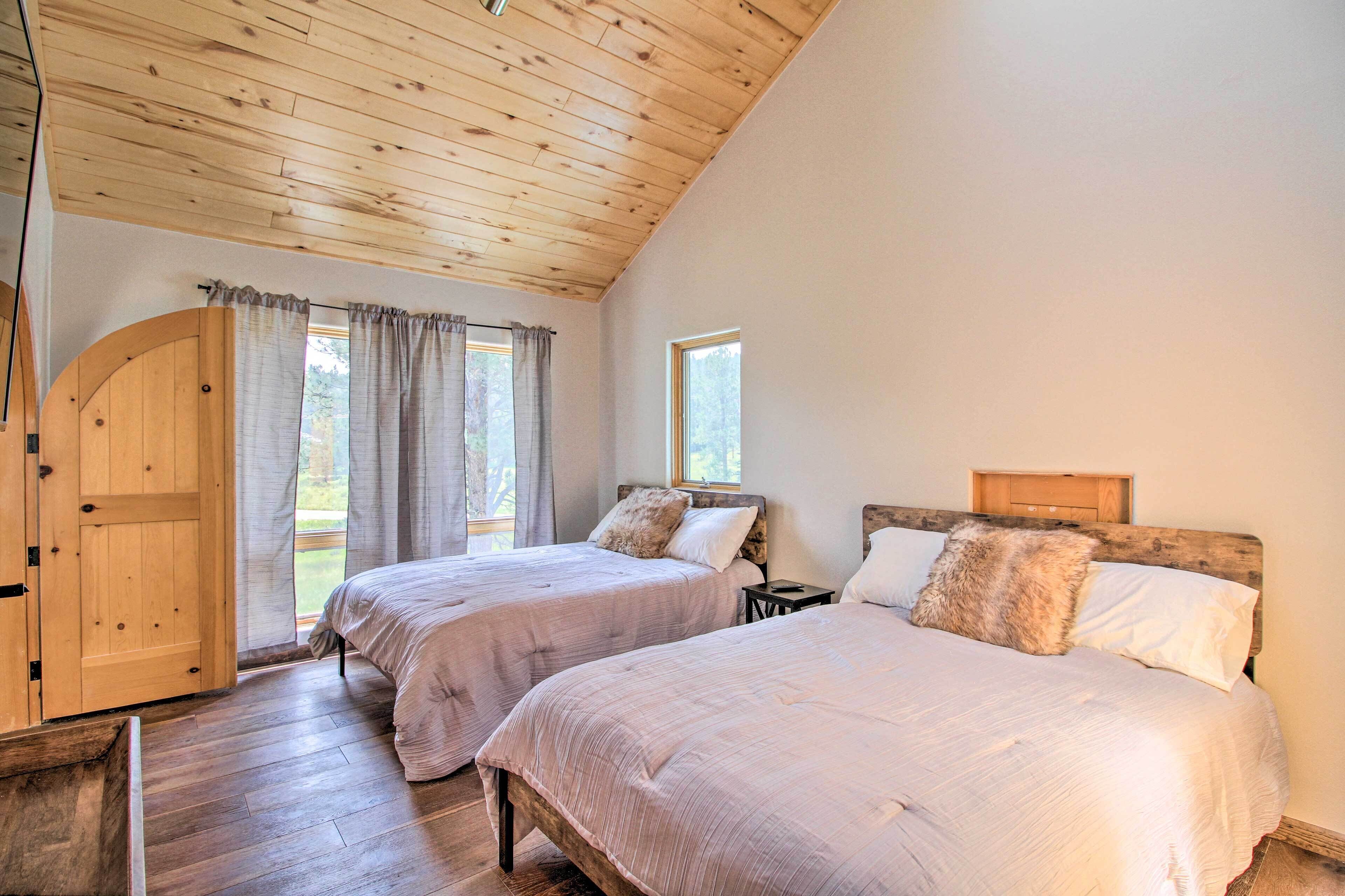 A bedroom with two beds, wooden ceiling, and a large window.