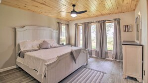 Ein Schlafzimmer mit Holzboden, einem Bett mit Kopfteil, einem Nachttisch, einer Kommode und einem Fenster mit Vorhängen.