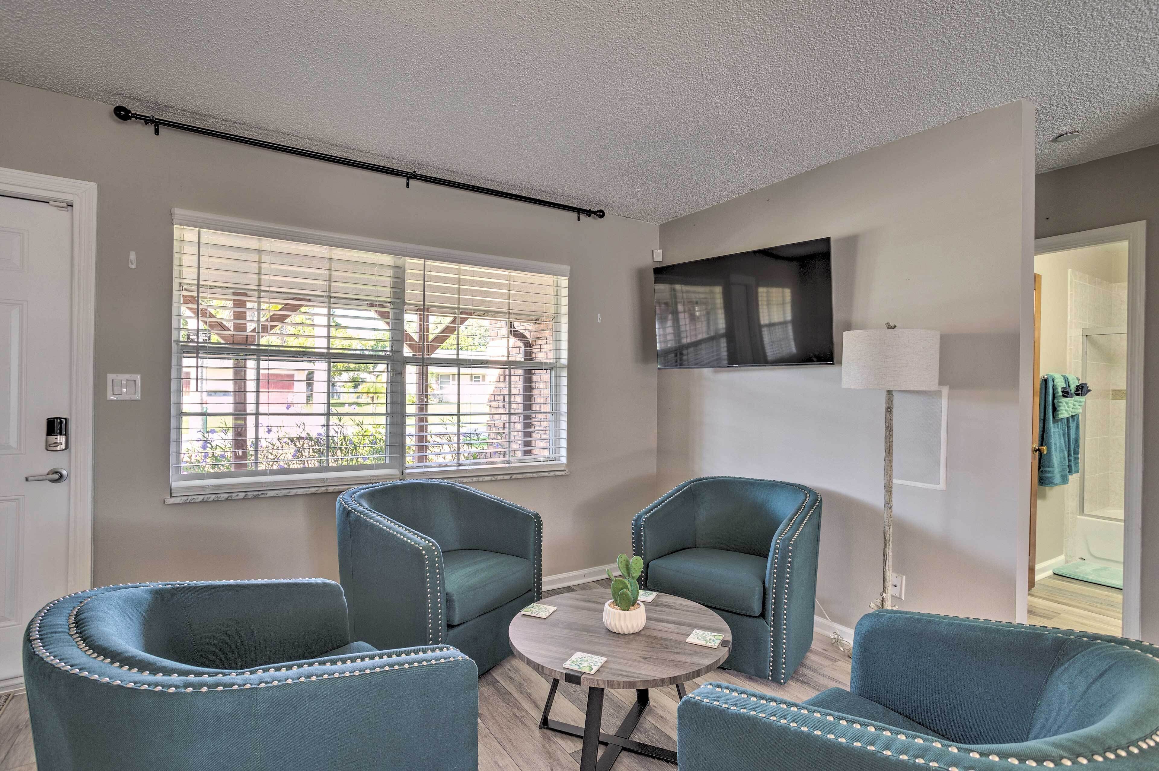 A room with two upholstered chairs, a small round table with a plant, and a television mounted on the wall.