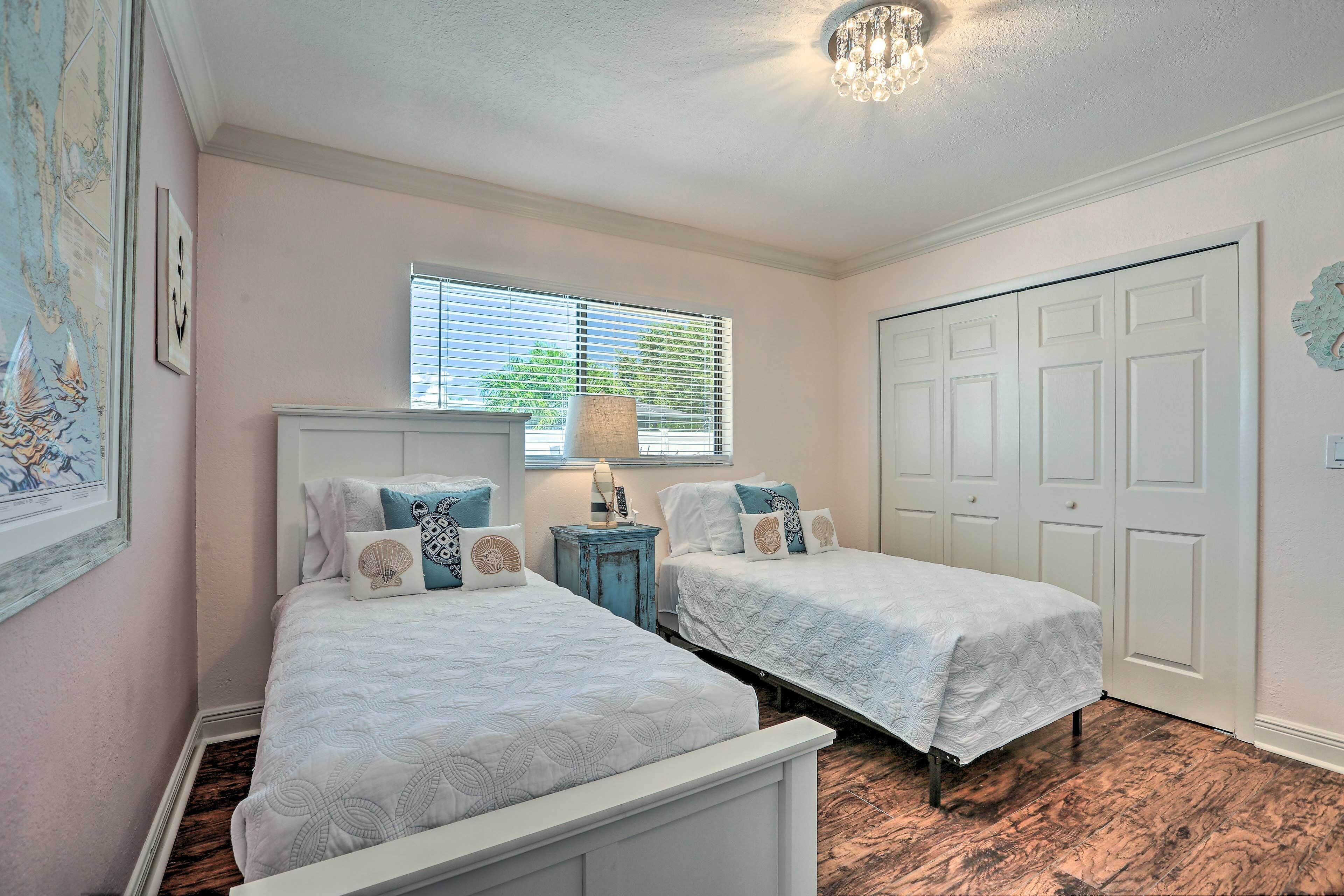 Un dormitorio con dos camas, una ventana con persianas, un candelabro y una puerta con un adorno decorativo.