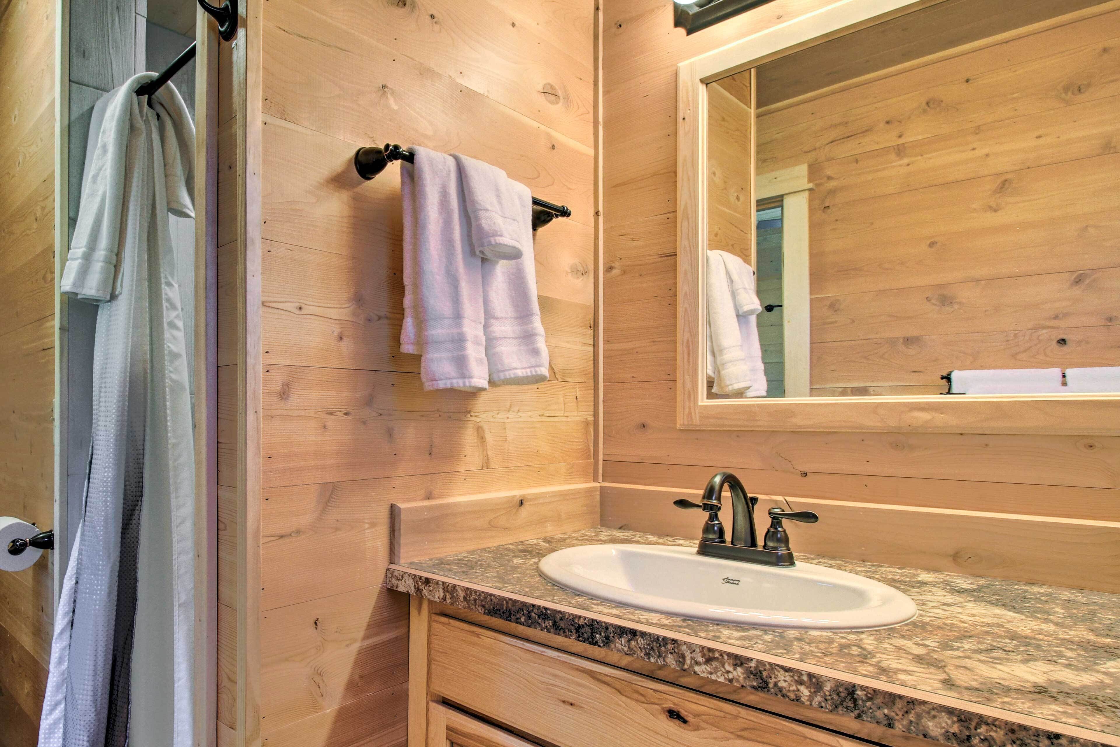 Une salle de bain aux murs lambrissés, dotée d’un lavabo avec un plan de travail en granit, d’un miroir et de deux serviettes suspendues à des crochets.
