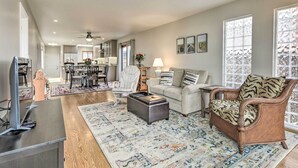 A spacious living room with a sofa, armchair, and ottoman, a dining area with a table and chairs, and a kitchen in the background. - Ideally Located San Francisco Bay Home w/ Sunroom! (Alameda)