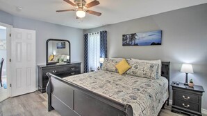 Une chambre à coucher avec un lit, une table de chevet, un miroir, un ventilateur de plafond et un tableau accroché au mur.
