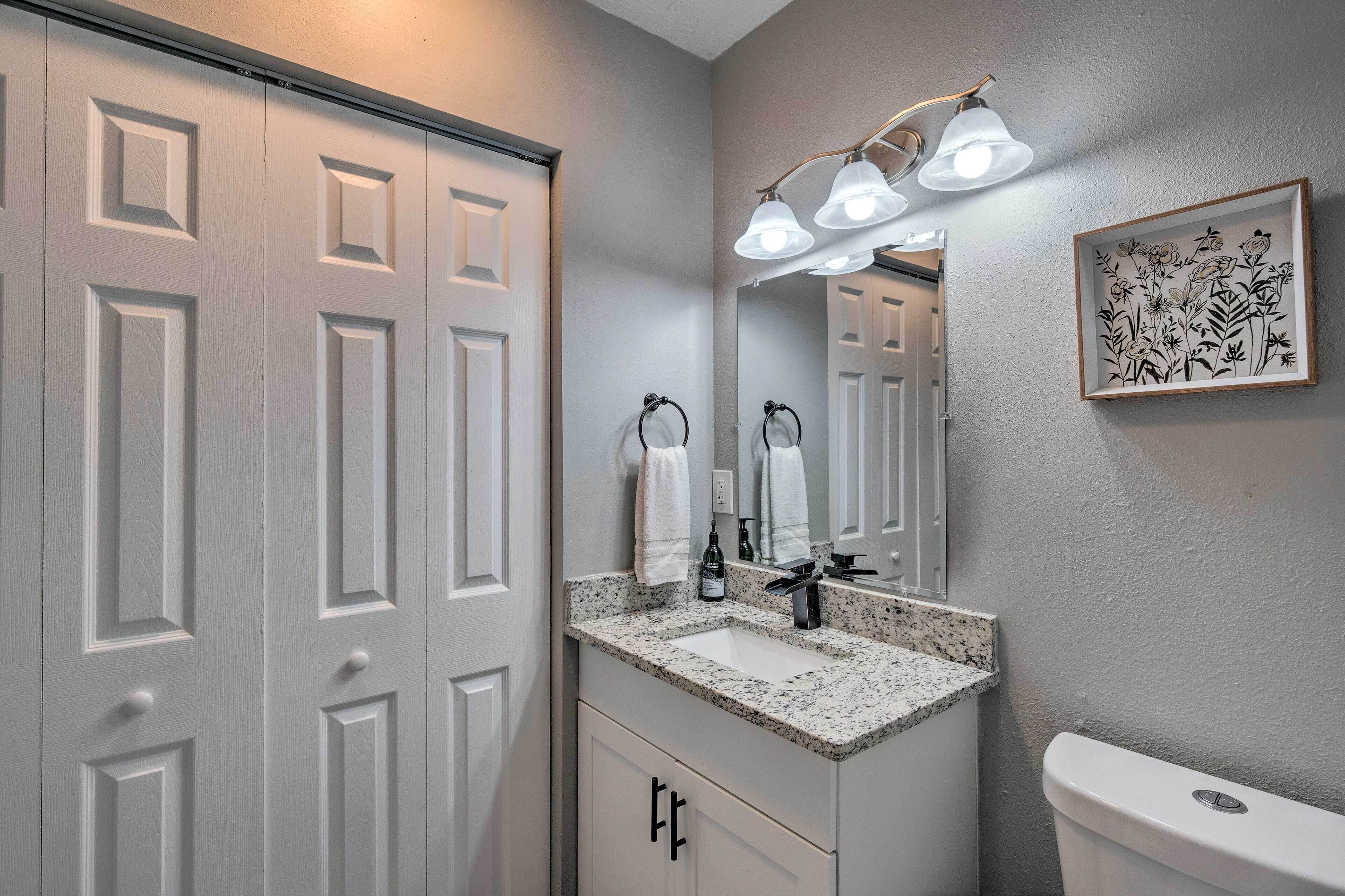 A bathroom with a white door, a sink with a faucet, a toilet, and a wall-mounted light fixture.