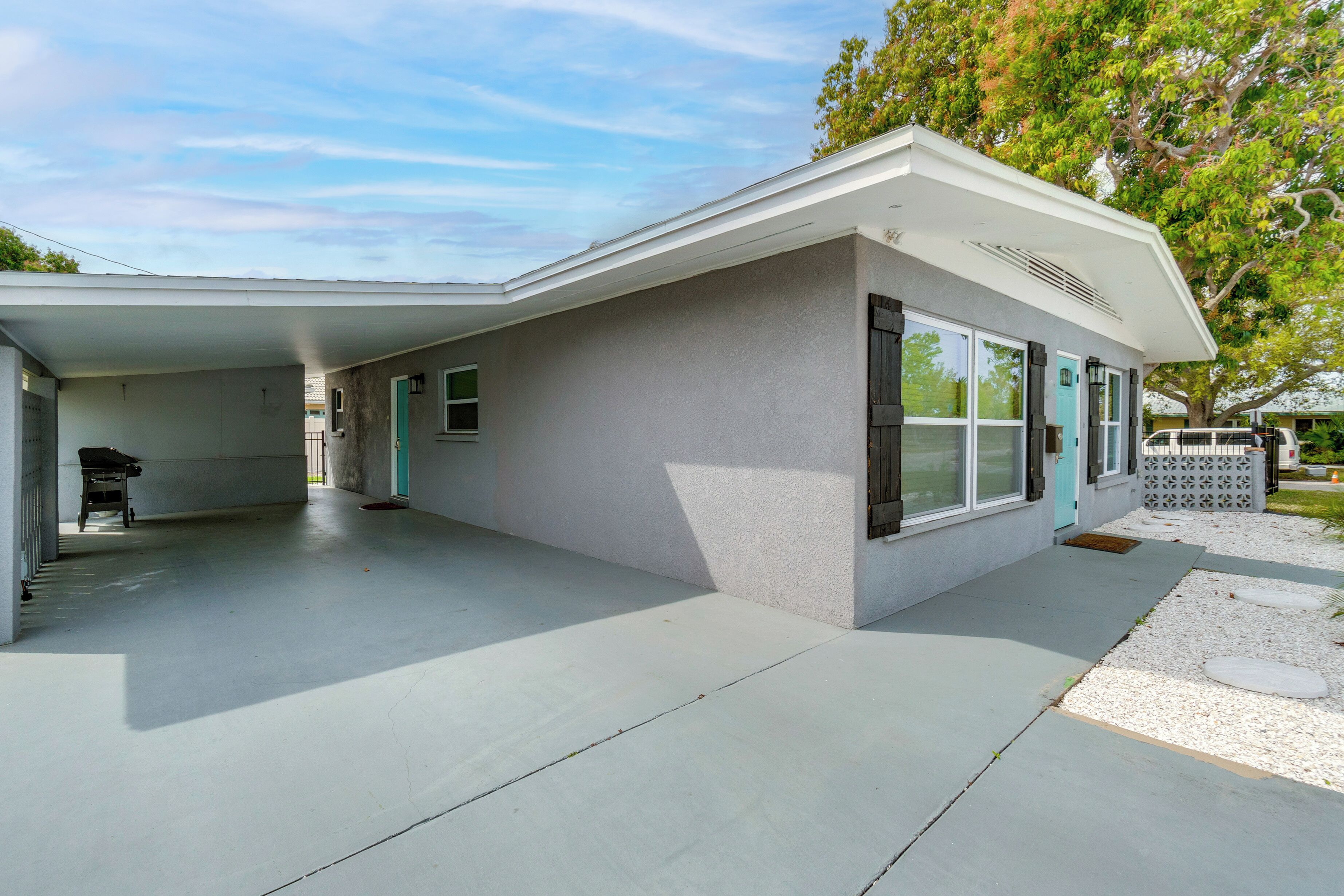 A modern single-story house with a covered patio area, a garage, and a front yard with a tree.