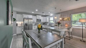A modern kitchen with white cabinets, stainless steel appliances, and a wooden dining table. - Bright Venice Getaway < 1 Mi to Historic Dtwn (Venice)