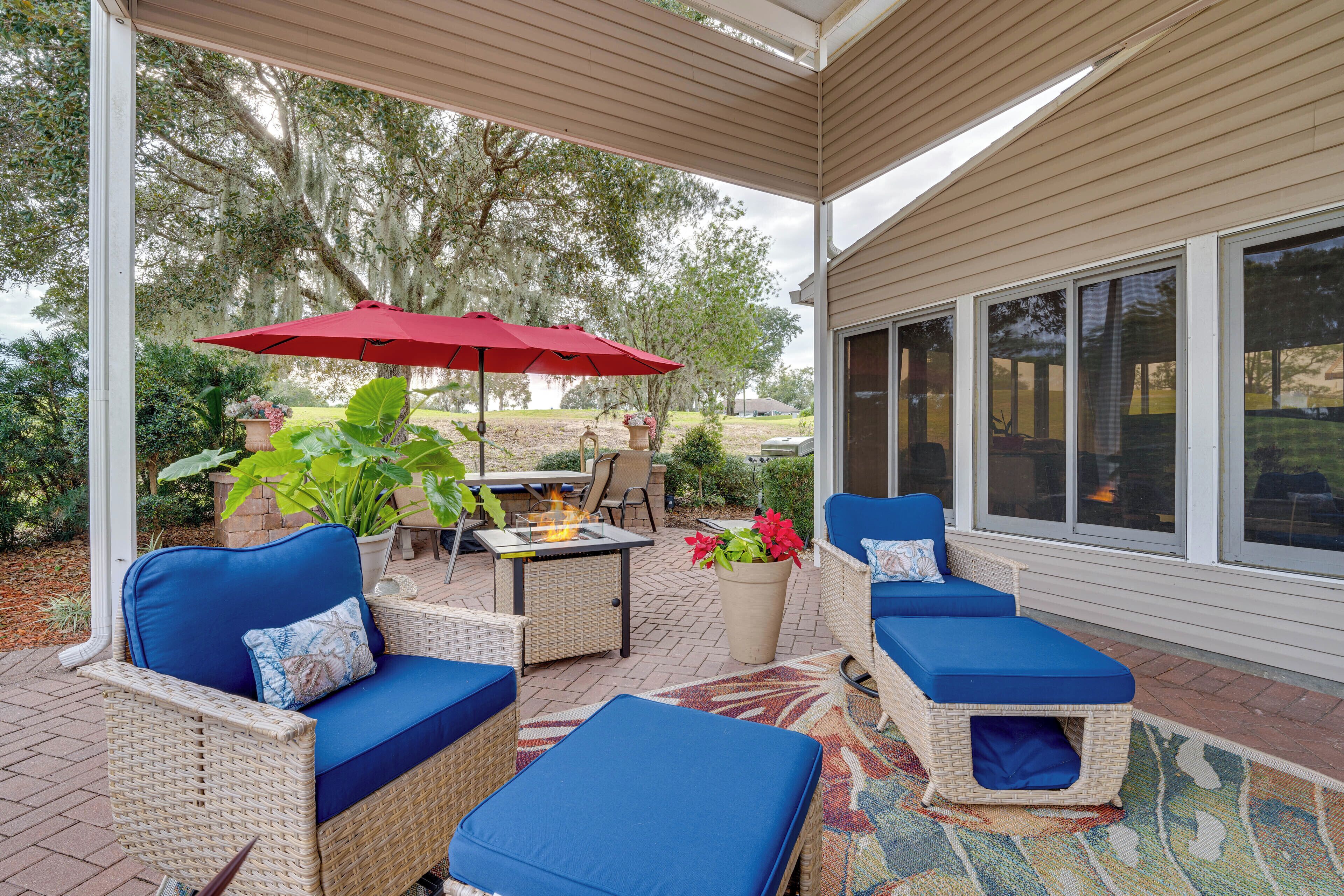 A covered patio with wicker furniture, a red umbrella, and a fire pit.