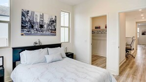 A bedroom with a bed, a nightstand, a wall-mounted bicycle, a framed picture, and a door leading to another room. - 4 Mi to Beach! San Juan Capistrano Home w/ Patio (San Juan Capistrano)