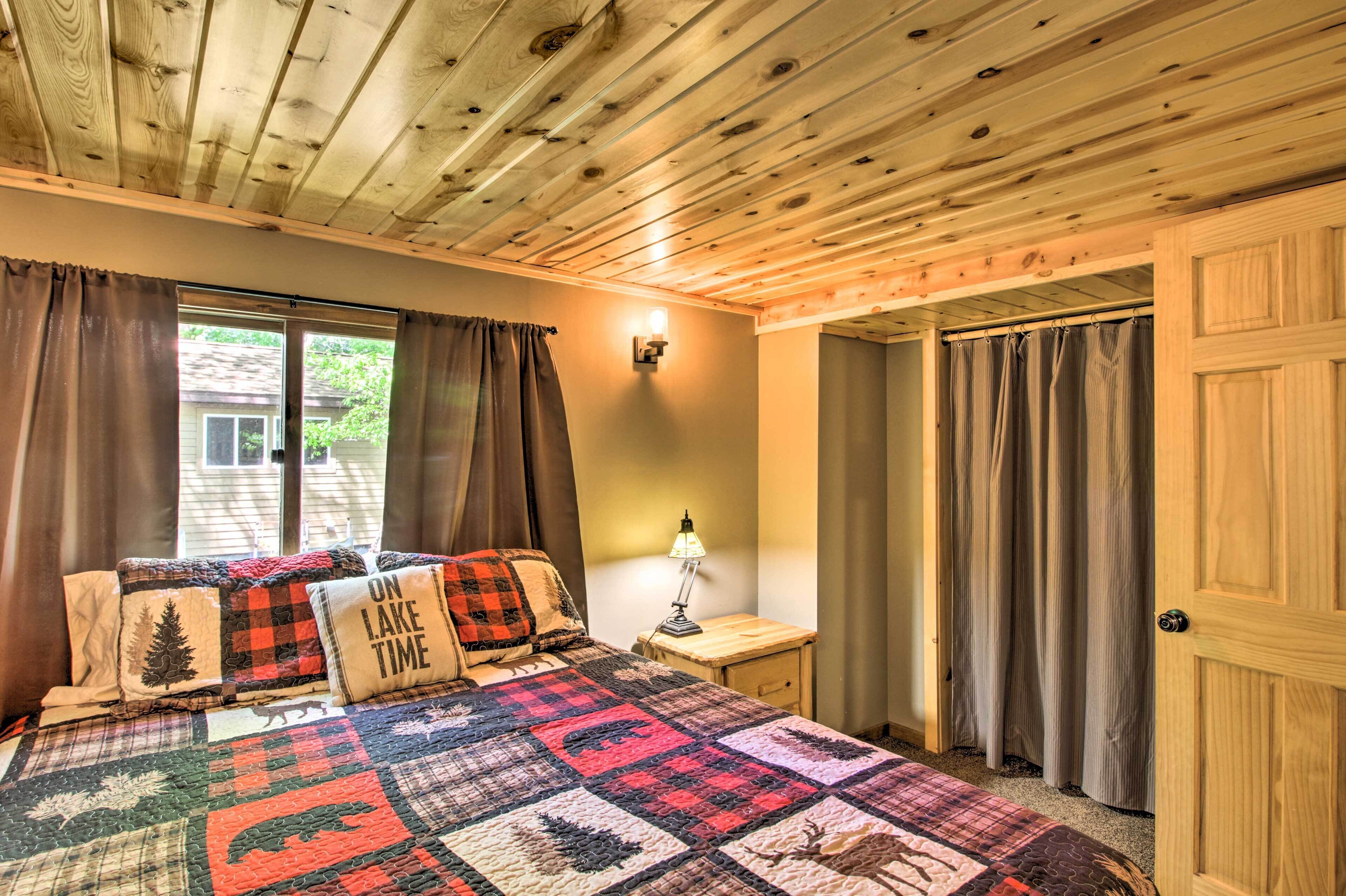 Een slaapkamer met een houten plafond, een bed met een quilt, een nachtkastje met een lamp en een deur.