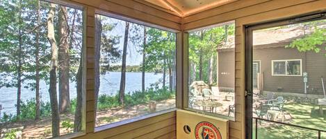 A wooden deck with large windows overlooking a lake, a paddleboard, and outdoor furniture.