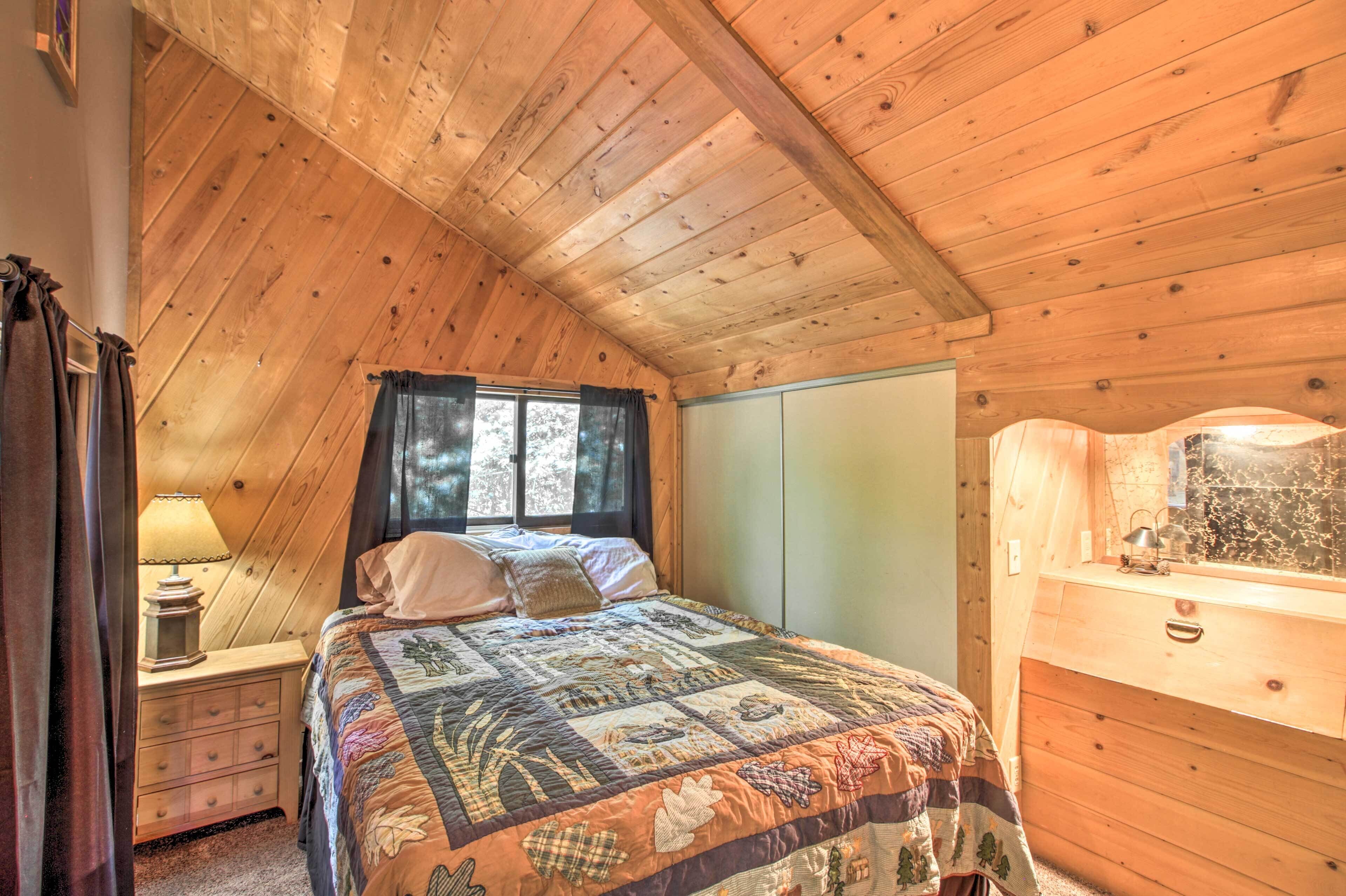 Een gezellige slaapkamer met een houten plafond, een bed met quilt, een nachtkastje met lamp en een dressoir.