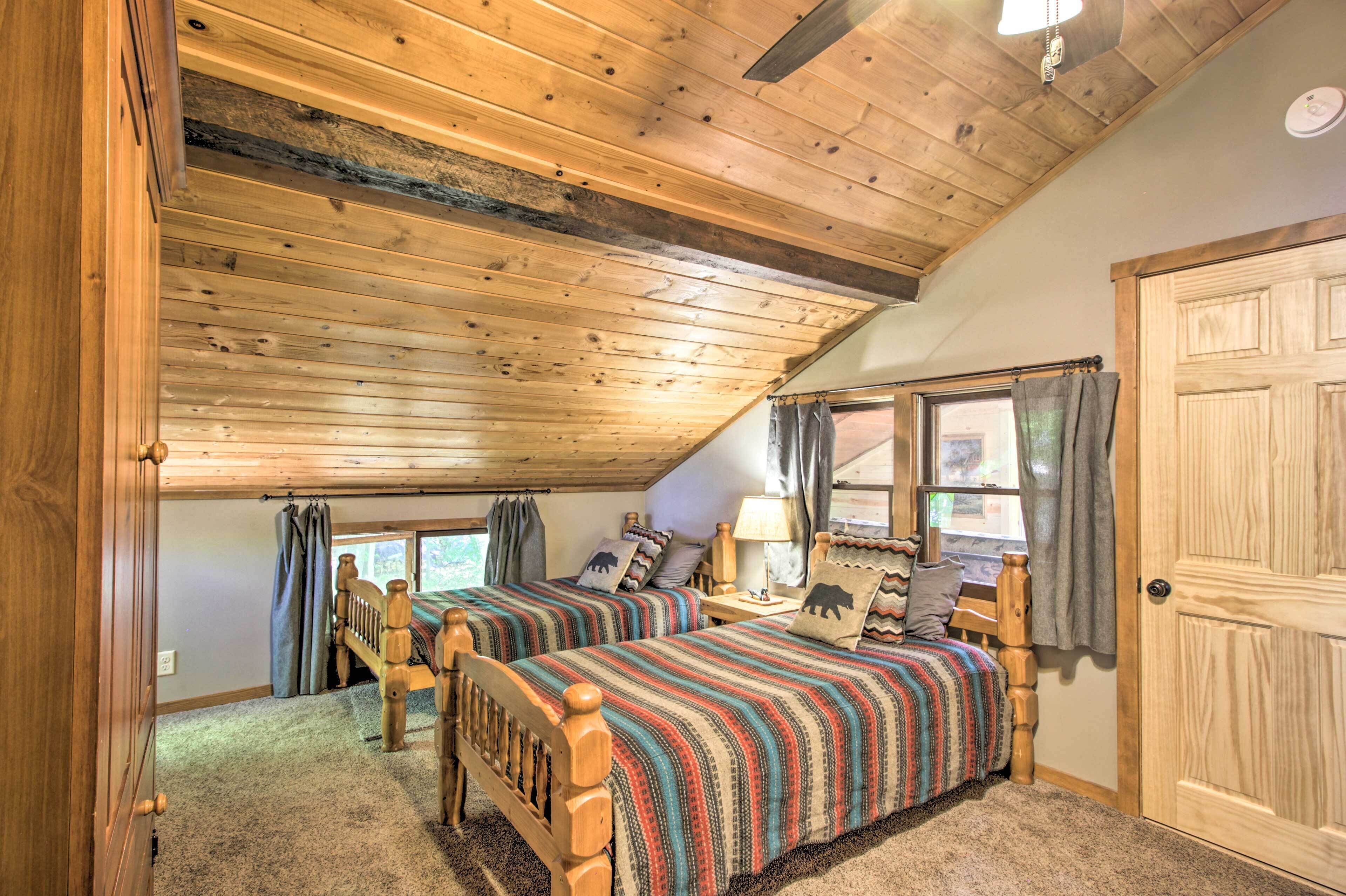 Une chambre avec deux lits en bois, un ventilateur de plafond et une grande fenêtre avec des rideaux.