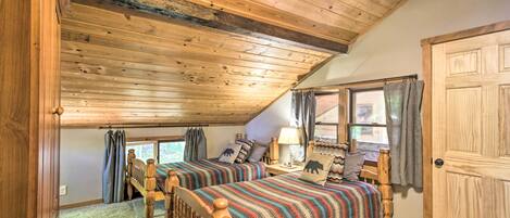 Une chambre avec deux lits en bois, un ventilateur de plafond et une grande fenêtre avec des rideaux.
