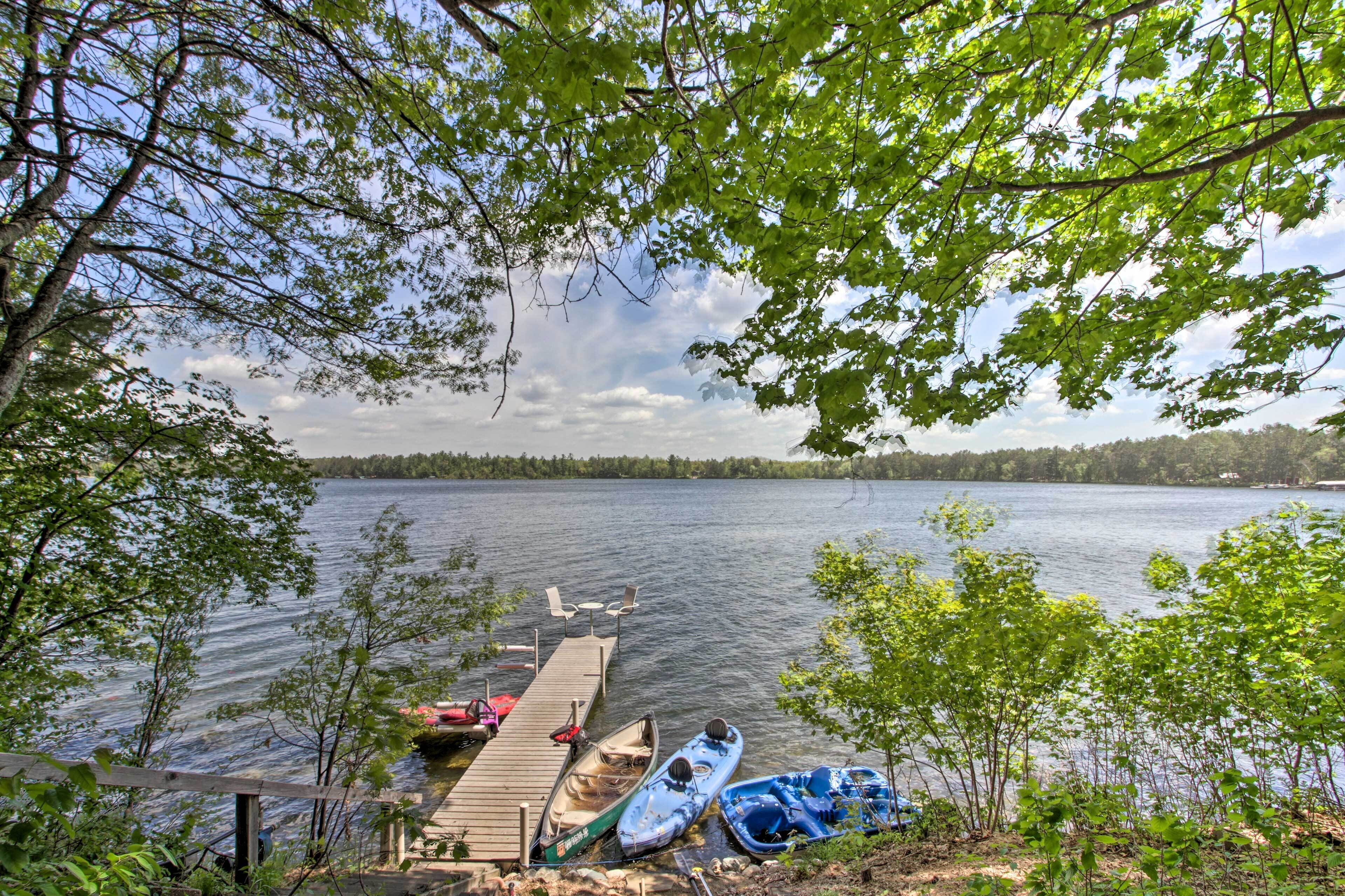 A dock with canoes and a rowboat, surrounded by trees and a lake.