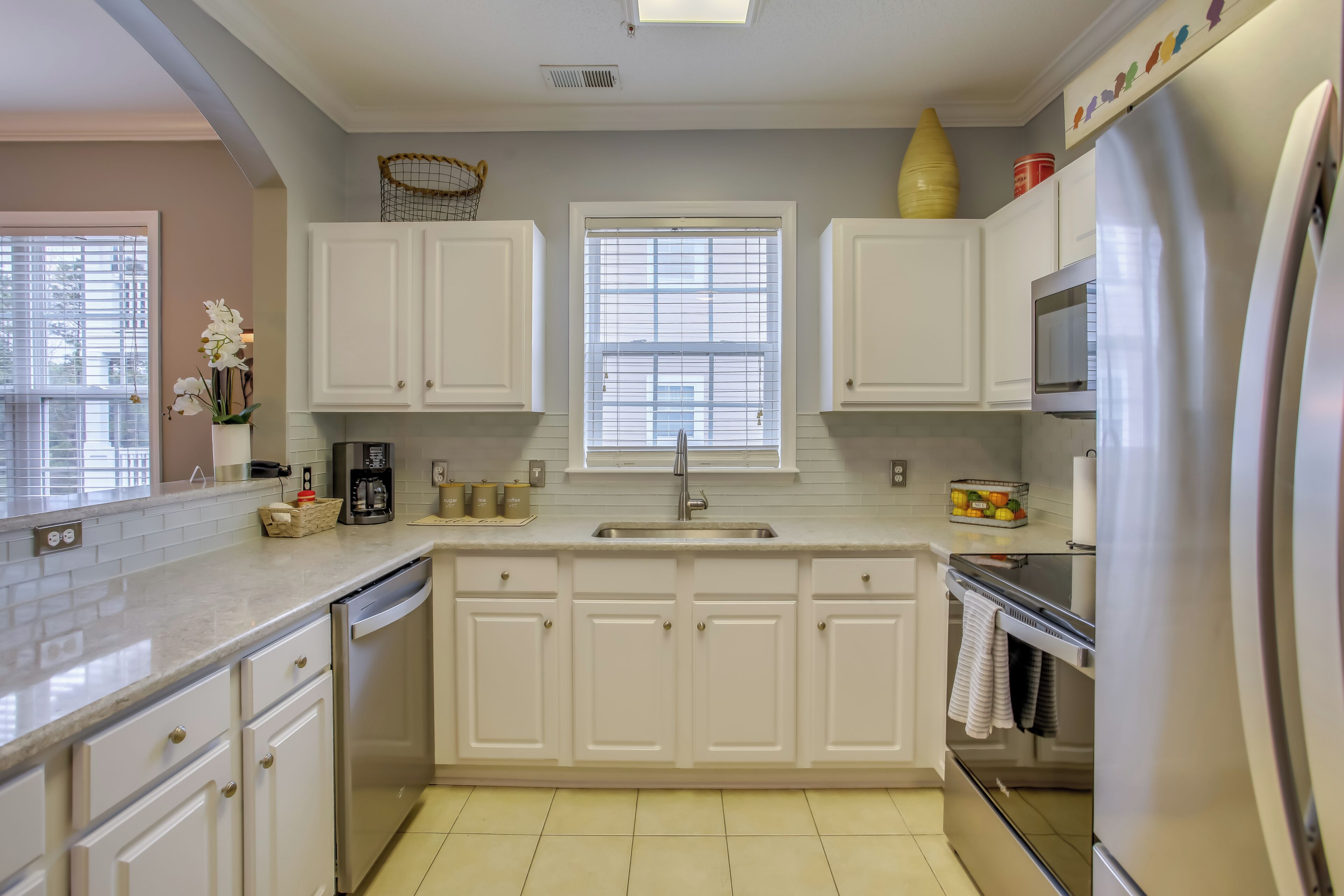 A kitchen with white cabinets, a stainless steel refrigerator, a microwave, and a sink.