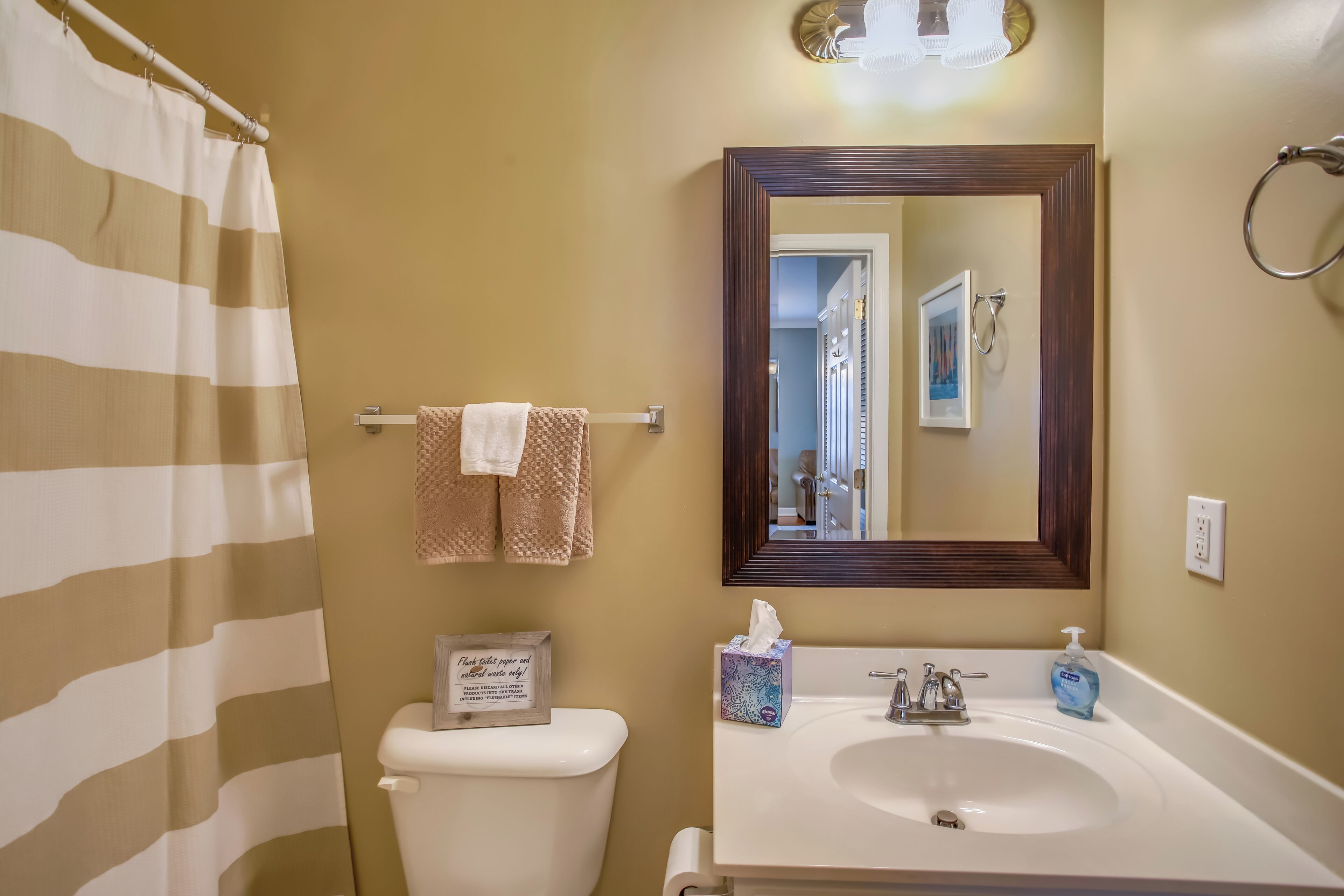 Ein Badezimmer mit gestreifter Duschvorhang, Toilette, Waschbecken mit Spiegel und Handtuchhalter.