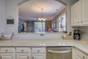 A kitchen with white cabinetry, a built-in dishwasher, and a large window. - Golf Resort Condo w/ Pool in North Myrtle Beach! (North Myrtle Beach)