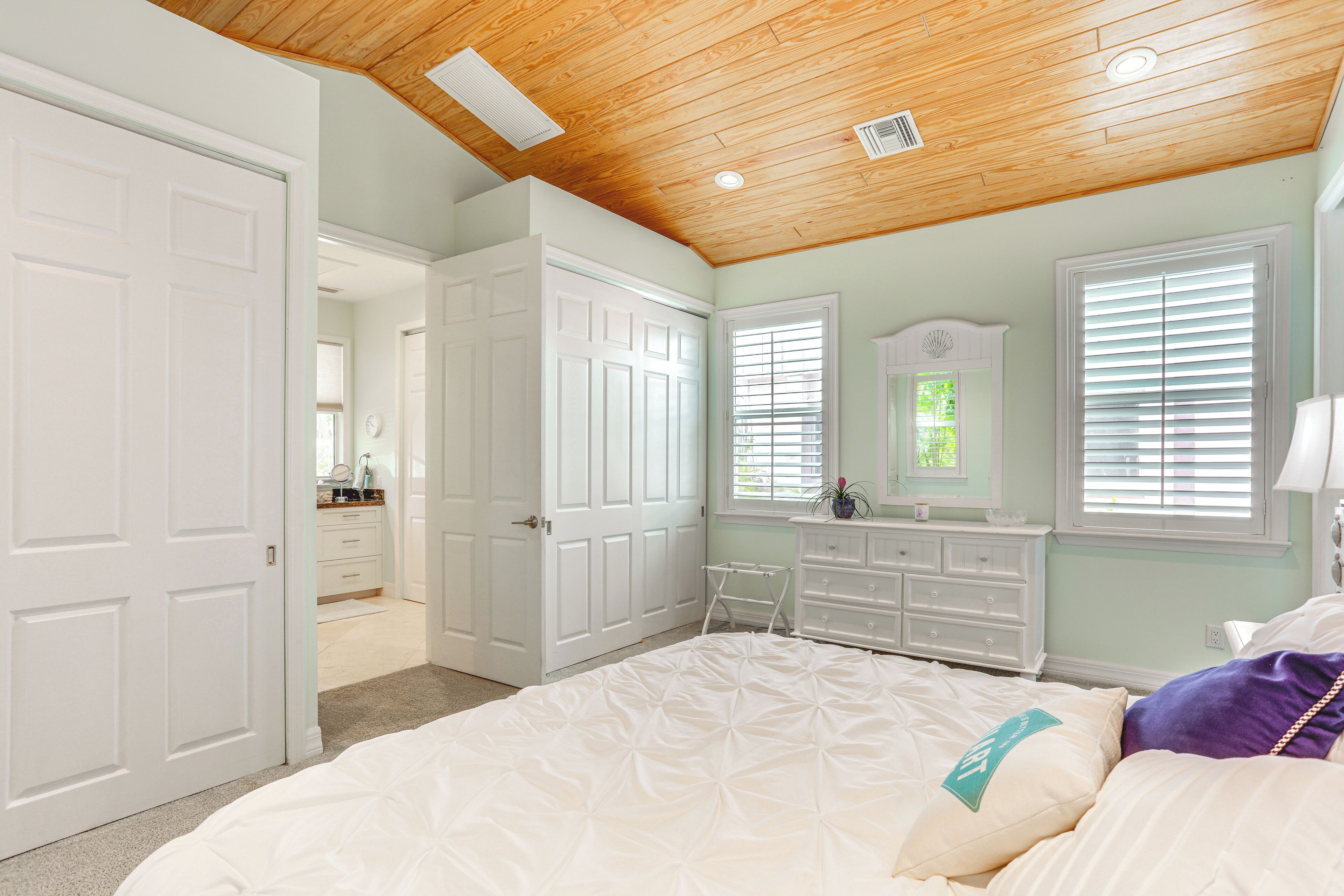 A bedroom with a large bed, white dresser, and a wooden ceiling.