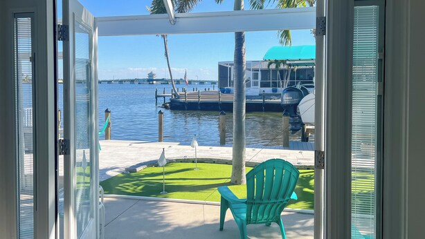 A view from a covered patio with a green chair, a dock, and boats in the background. - Matlacha Waterfront Retreat: Dock & Hot Tub! (Matlacha)