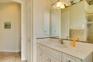 A bathroom with a white sink, mirror, and cabinets. There are light switches on the wall, and a painting on the wall. - WFH & Relax by Pool: Chic Cape Coral Villa (Cape Coral)