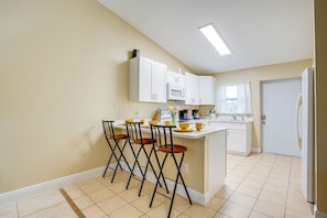 A kitchen with white cabinets, a central island with stools, a microwave, and a refrigerator.