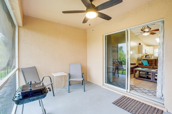 A balcony with a ceiling fan, a chair, a table, and a view into the living room.