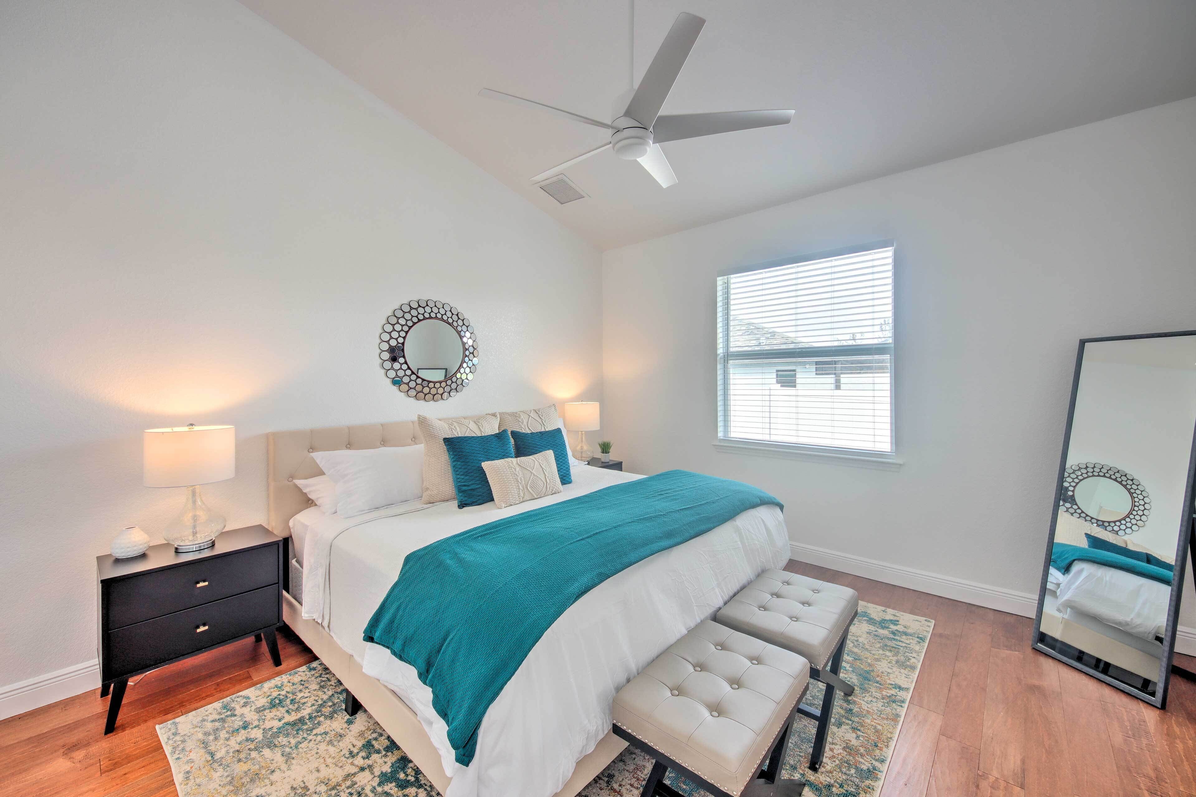 A bedroom with a bed, bedside table, lamp, bench, and a ceiling fan.