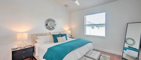 A bedroom with a bed, bedside table, lamp, bench, and a ceiling fan.