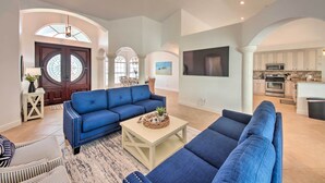 A spacious living area with a blue sectional sofa, a coffee table, and a dining area with a kitchen in the background. - On Canal: Luxe Cape Coral Oasis w/ Pool & Lanai! (Cape Coral)